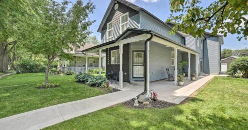A charming two-story house with a porch, surrounded by greenery and a well-maintained lawn on a sunny day.