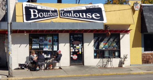 A colorful restaurant exterior with a sign reading "Bourbon Toulouse," featuring outdoor seating and patrons at tables.