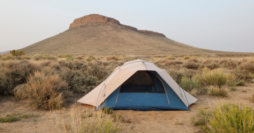A tent set up in a desert landscape with a large, flat-topped mountain in the background.