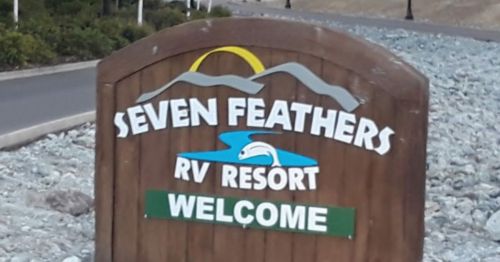 Wooden sign for Seven Feathers RV Resort, featuring a blue river and mountains, with "Welcome" in green.