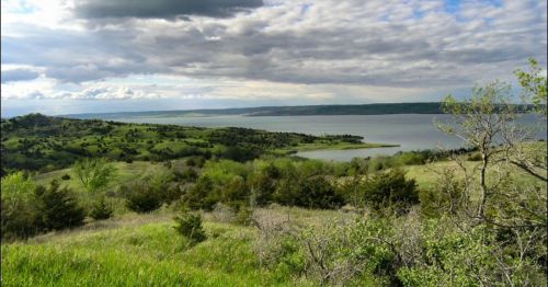 A scenic view of rolling green hills and a calm lake under a cloudy sky.