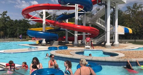 A vibrant water park scene with colorful slides, children playing in the pool, and adults relaxing nearby.