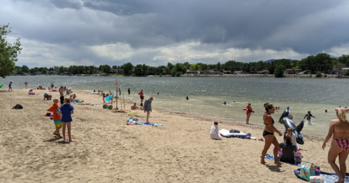A sandy beach with people enjoying the water, swimming, and relaxing under a cloudy sky.