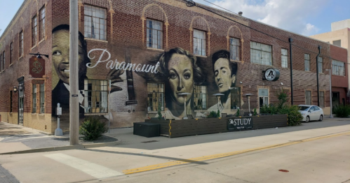 Mural on a brick building featuring black-and-white portraits of iconic actors, with a sign for "Study" in front.