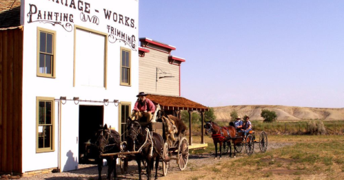 Two horse-drawn carriages outside a historic building labeled "Heritage Works" in a rural landscape.