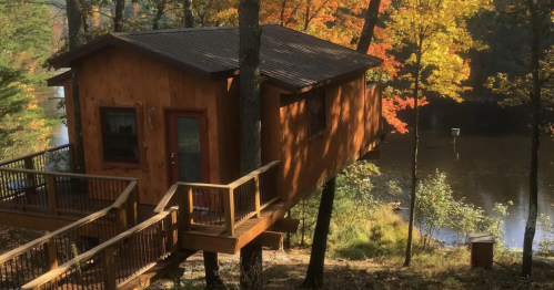 A wooden treehouse perched among trees, overlooking a serene lake surrounded by autumn foliage.