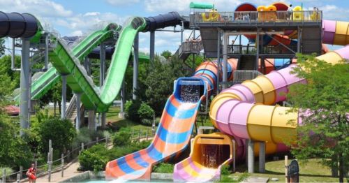 Colorful water slides in a park, featuring green, pink, and orange slides surrounded by greenery and blue skies.