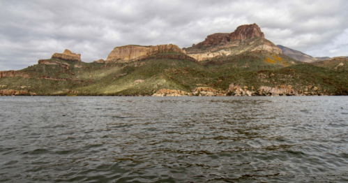 A scenic view of rugged mountains rising above a calm lake under a cloudy sky.