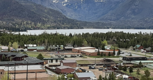 A scenic view of a small town by a lake, surrounded by mountains and lush greenery.
