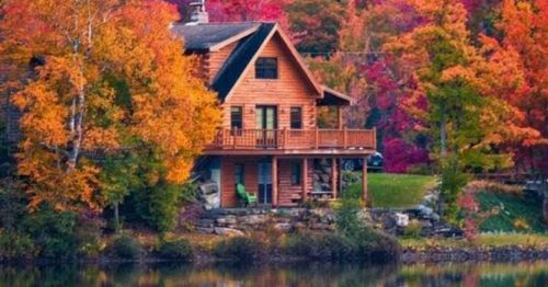 A cozy wooden cabin surrounded by vibrant autumn foliage and a calm lake reflecting the colorful trees.