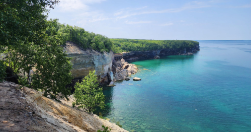 A scenic view of a rocky coastline with clear turquoise water and lush green trees under a blue sky.