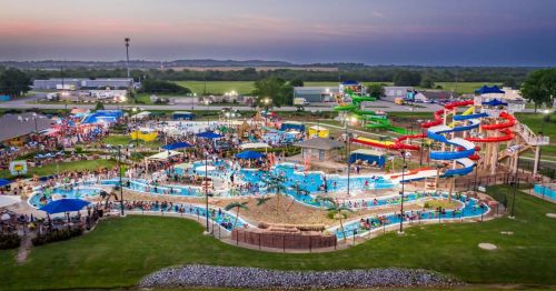 Aerial view of a busy water park with colorful slides, pools, and crowds enjoying the attractions under a sunset sky.