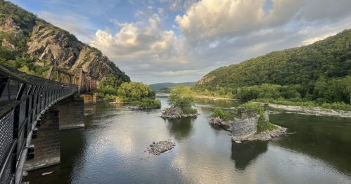 A scenic view of a river surrounded by lush green hills and rocky islands, with a bridge in the foreground.