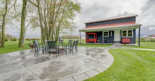 A modern house with a red roof, surrounded by trees, features a patio with a fire pit and outdoor seating.