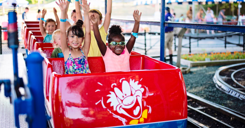 Children joyfully raise their hands on a colorful amusement park ride, smiling and enjoying the fun.