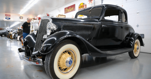 A classic black coupe car with whitewall tires, displayed in a vintage car museum.