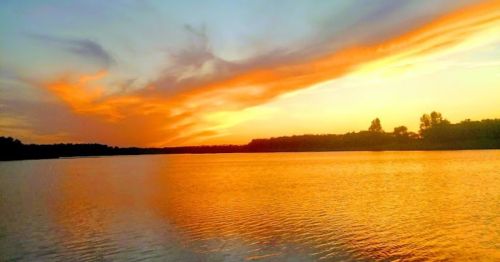 A serene sunset over a calm lake, with vibrant orange and blue hues reflecting on the water's surface.
