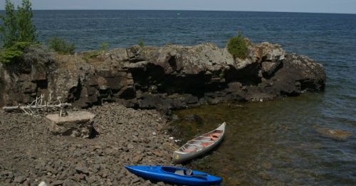 A rocky shoreline with two kayaks, one blue and one red, resting on the pebbled beach by the water's edge.