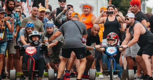 A crowd watches as two competitors prepare to race on large tricycles, with excitement and energy in the air.