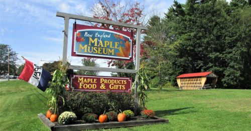 Sign for the New England Maple Museum, featuring maple products, food, and gifts, surrounded by autumn decorations.