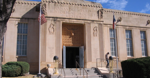 Exterior of the Panhandle-Plains Historical Society Museum, featuring stone architecture and flags, under a blue sky.