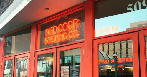 Bright red storefront of Red Door Brewing Co. with an "OPEN" sign and large windows showcasing the interior.