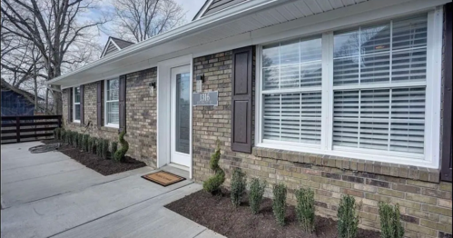 Exterior view of a brick house with a front door, windows, and neatly trimmed shrubs along the walkway.
