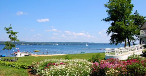 A scenic lakeside view with colorful flowers in the foreground, boats on the water, and a clear blue sky.