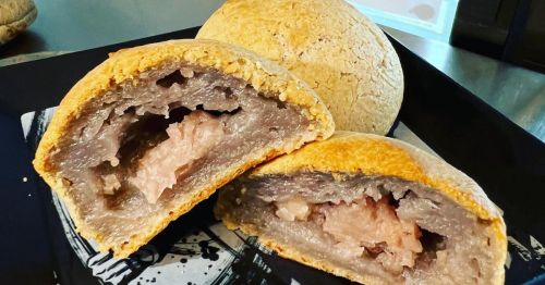 A close-up of a baked pastry, cut in half, revealing a pink filling inside a golden-brown crust.