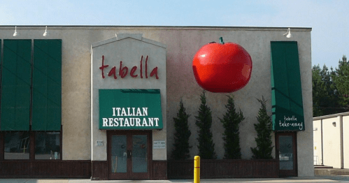 Exterior of an Italian restaurant named "Tabella," featuring a large red tomato sculpture above the entrance.