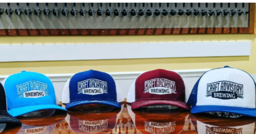 A row of colorful caps with "Craft Advisory Brewing" logo displayed on a wooden surface.