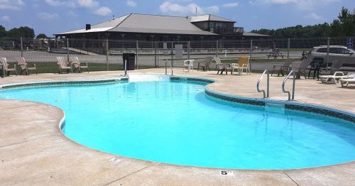 A clear blue swimming pool with lounge chairs around it, set against a building and a sunny sky.