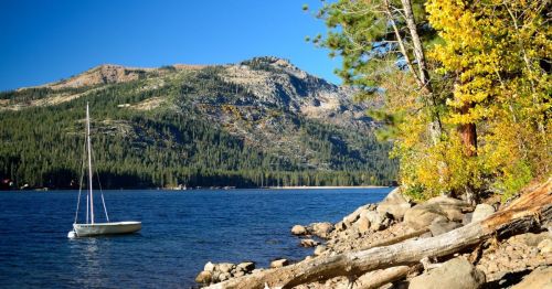A serene lake scene with a sailboat, rocky shore, and colorful autumn trees against a mountain backdrop.