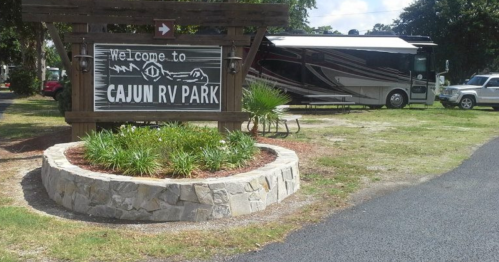 Sign for Cajun RV Park with an RV and greenery in the background, welcoming visitors to the park.