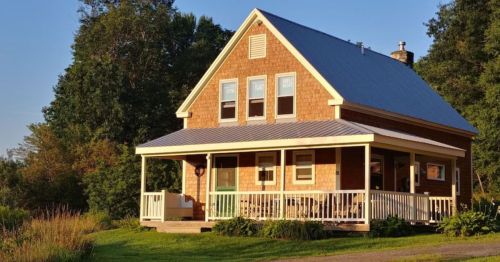 A charming two-story house with a porch, surrounded by greenery and bathed in warm sunlight.