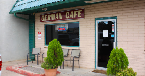Exterior of a German cafe with a sign reading "OPEN," featuring potted plants and outdoor seating.