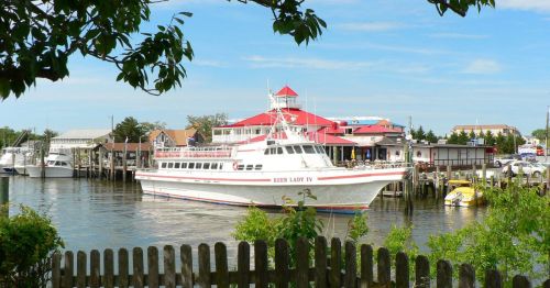 A white boat named "Keen Lady IV" docked near a waterfront restaurant and other boats under a clear blue sky.