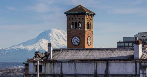 Historic clock tower with a snow-capped mountain in the background under a clear blue sky.