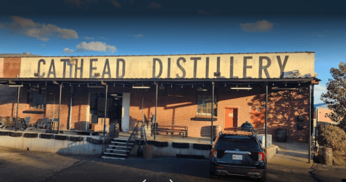 Exterior of Cathead Distillery, featuring a brick building with large signage and a parked vehicle in front.