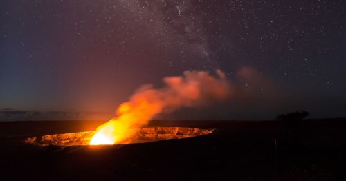 A glowing volcano erupts at night, with a starry sky in the background and smoke rising from the crater.