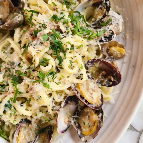 A close-up of pasta with clams, topped with parsley and grated cheese, served in a white bowl.