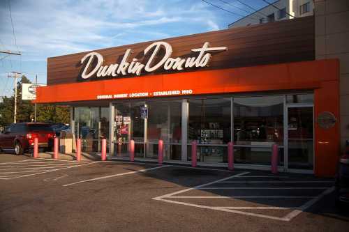 Exterior of a Dunkin' Donuts store with a large sign, parking spaces, and pink bollards in front.