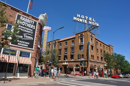 Historic buildings on a sunny street in Flagstaff, Arizona, featuring Hotel Monte Vista and Babbitt Brothers storefront.