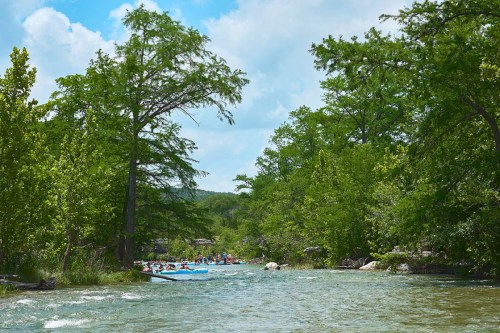 A serene river scene surrounded by lush green trees, with people kayaking and enjoying the outdoors.