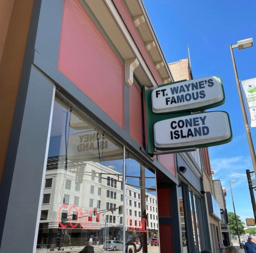 Sign for "Ft. Wayne's Famous Coney Island" on a building, with reflections of the street visible in the windows.
