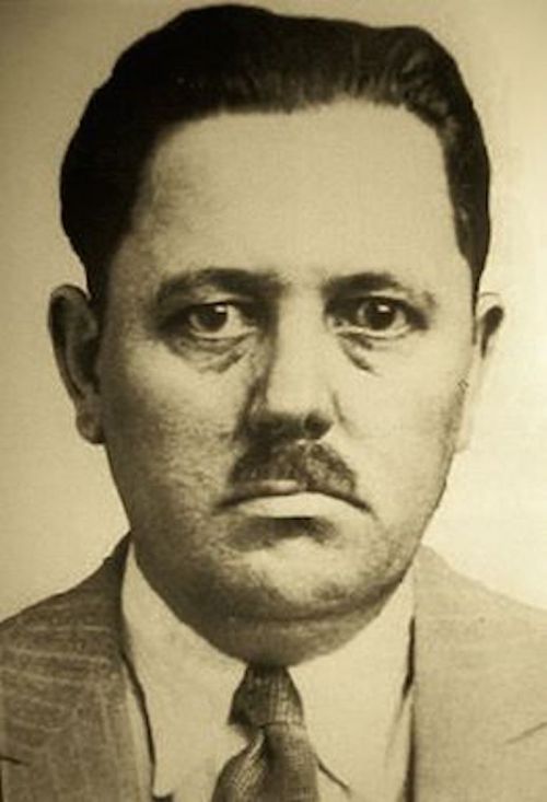 Black and white portrait of a man with a mustache, wearing a suit and tie, looking directly at the camera.