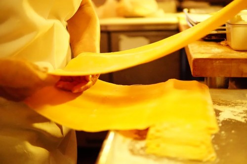 A chef skillfully stretches a sheet of fresh pasta in a kitchen setting.