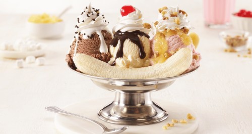 A banana split with three scoops of ice cream, topped with whipped cream, nuts, chocolate, and a cherry.