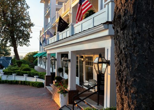 A charming hotel entrance with American flags, lanterns, and lush greenery, bathed in warm evening light.