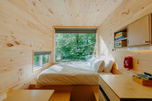 Cozy wooden bedroom with a large window, natural light, and minimalist decor, featuring a bed and a small desk.